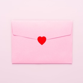 Envelope Sealed With Red Colored Heart Sticker on Pink Colored Background.