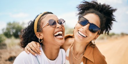 Friends hug and laugh outdoros during summer vacation.